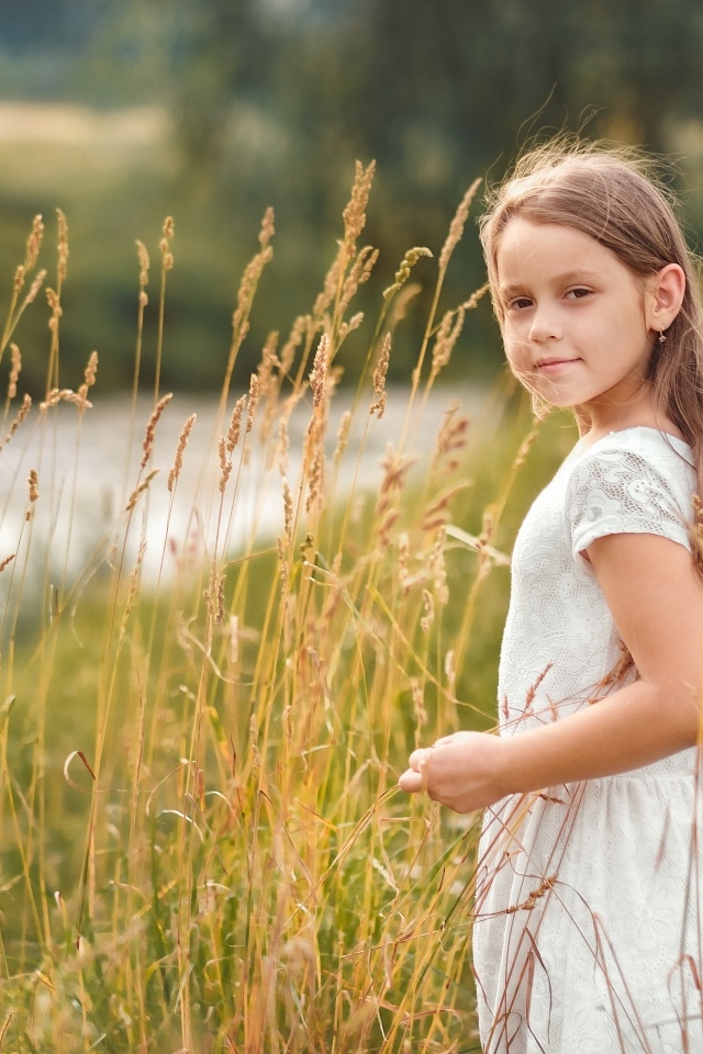 Маленькая девочка в белом платье гуляет по высокой траве