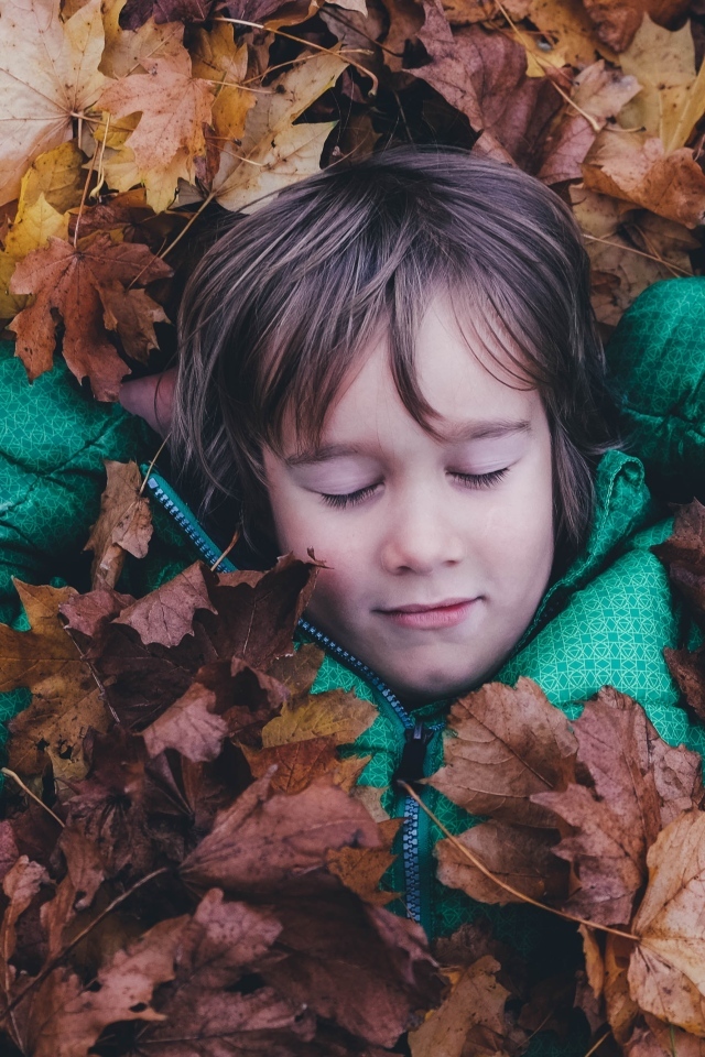 Маленькая девочка с закрытыми глазами лежит в сухой листве
