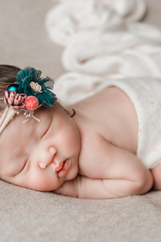 Новорожденная девочка азиатка спит на сером покрывале