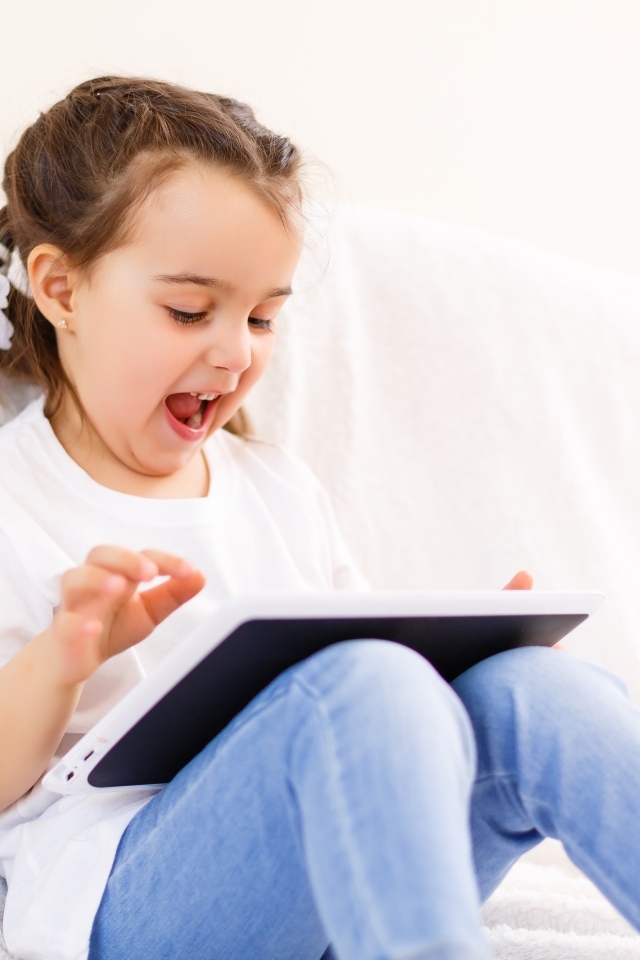 Веселая девочка с планшетом на кровати 