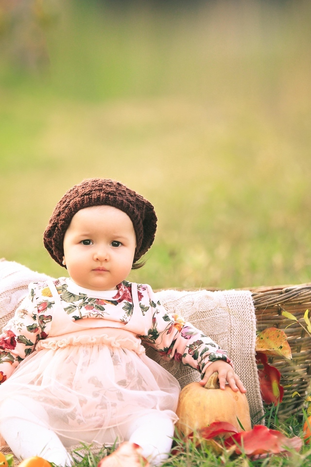 Милая маленькая девочка в шапке сидит на траве 