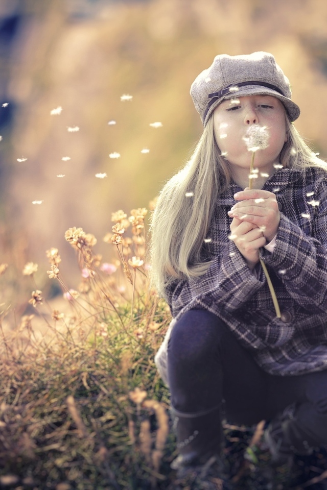 Девочка в кепке сдувает одуванчик