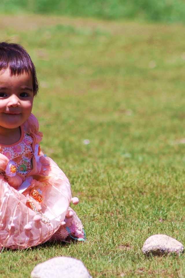 Девочка в розовом платье играет на зеленой траве