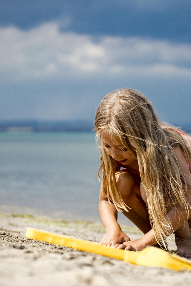 Девочка играет на песке у моря