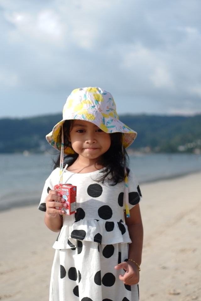 Девочка с соком в руках стоит на пляже