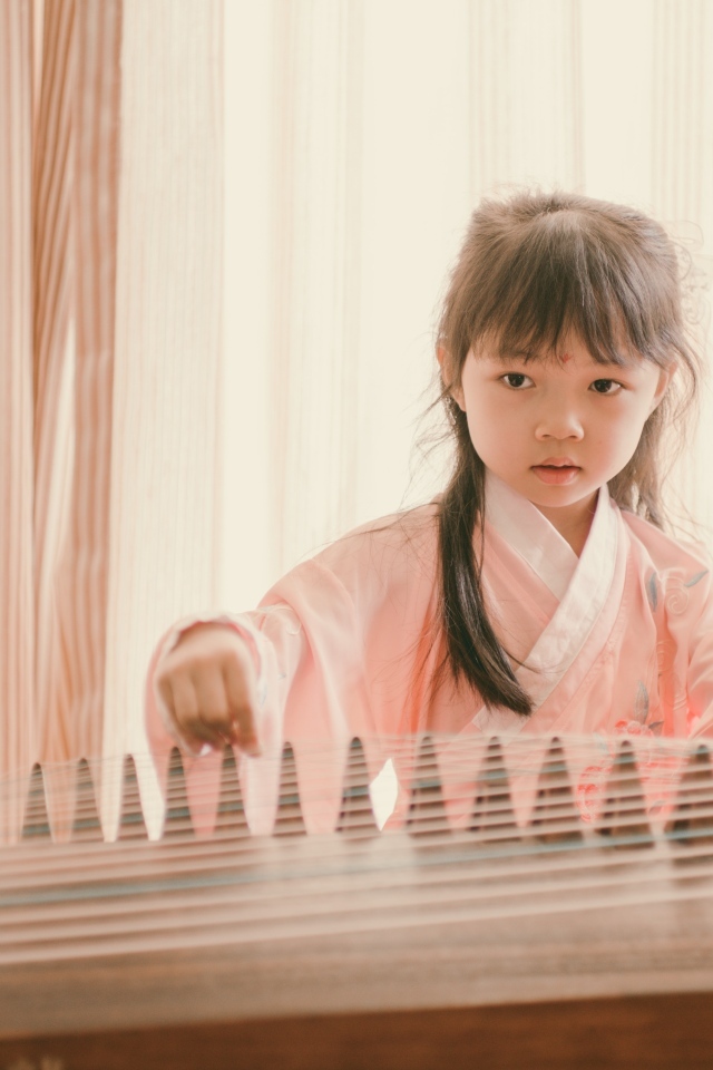 Маленькая девочка азиатка играет на музыкальном инструменте