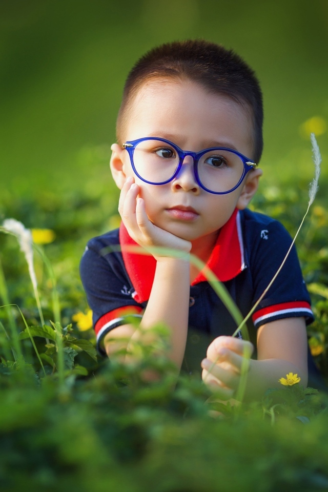 Маленький мальчик в очках лежит на траве