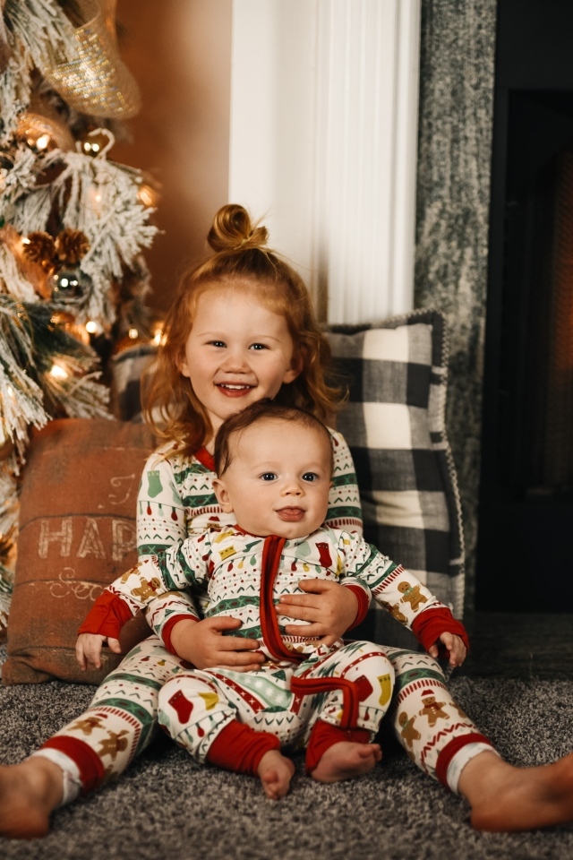 Маленькие брат и сестра сидят у новогодней ели