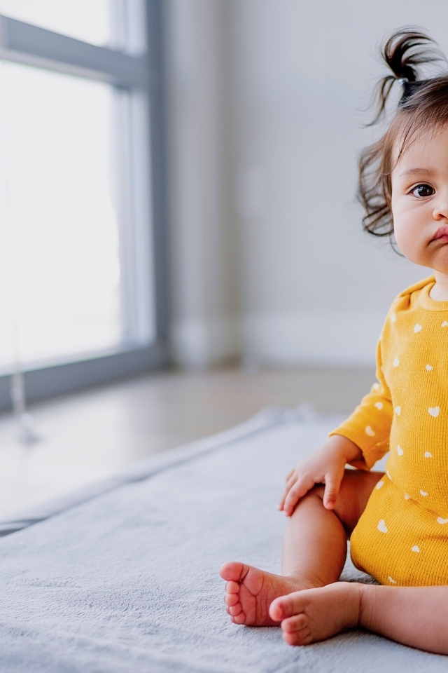 Маленькая смешная девочка сидит у окна