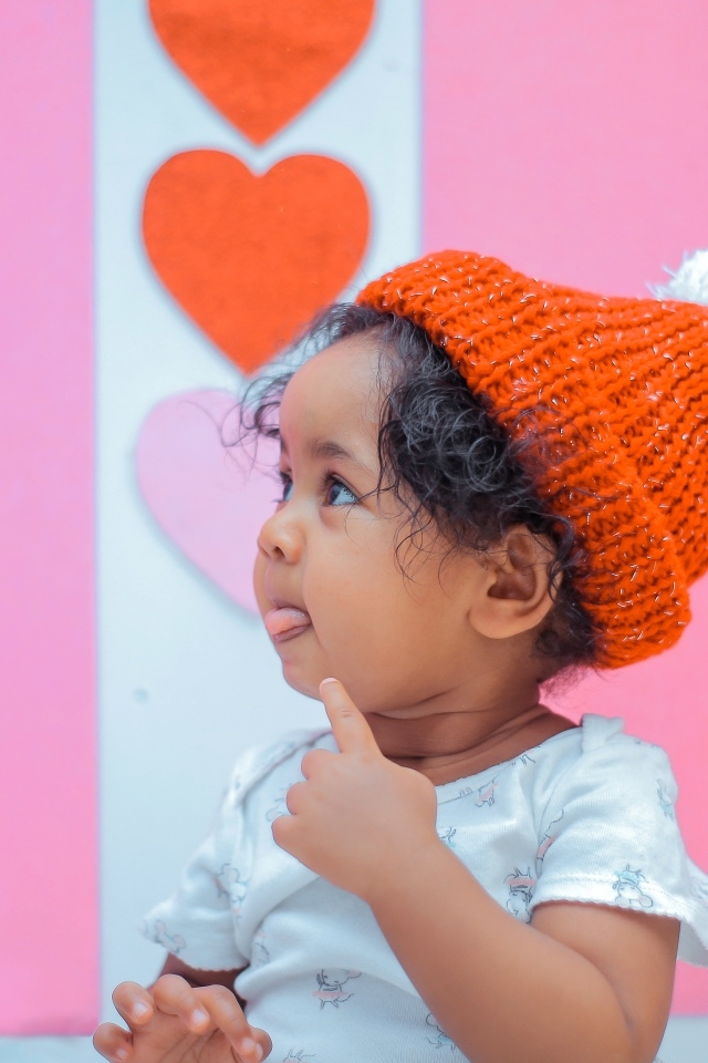 Маленькая девочка в вязаной шапке на розовом фоне