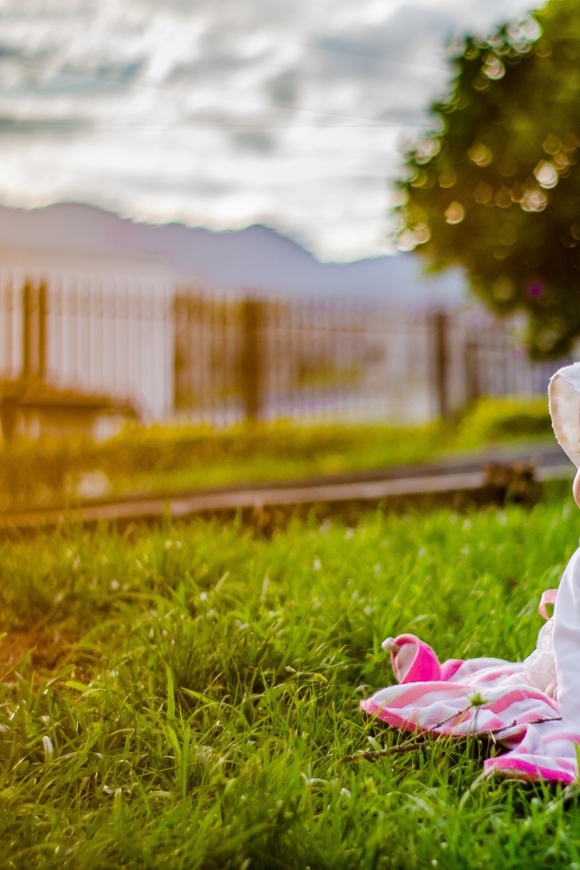 Маленькая девочка в розовом платье сидит на траве