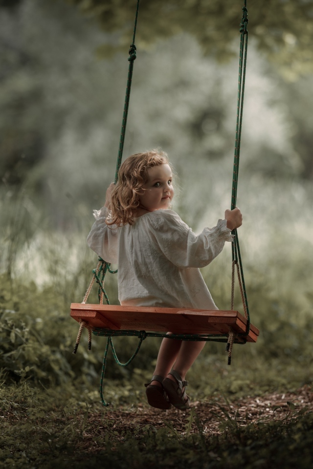 Маленькая девочка на качели в саду