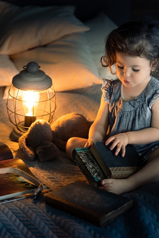 Маленькая девочка читает книги на кровати