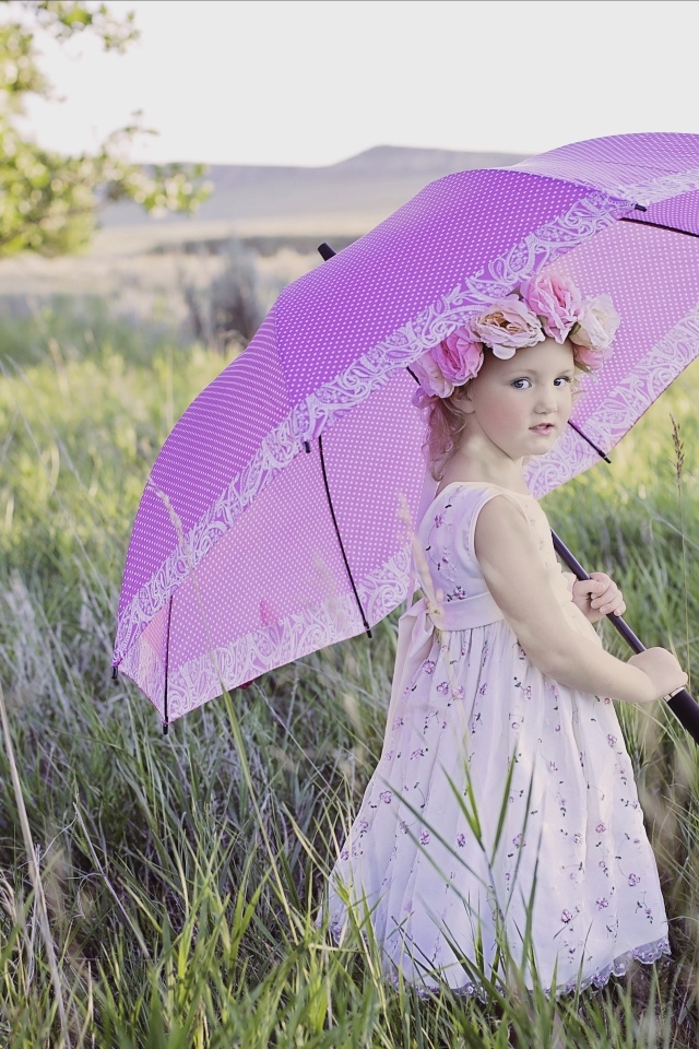 Маленькая девочка стоит в траве с зонтом