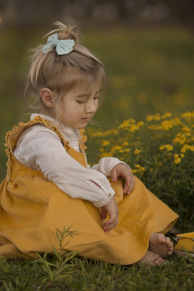 Маленькая девочка с игрушечной машиной сидит на траве