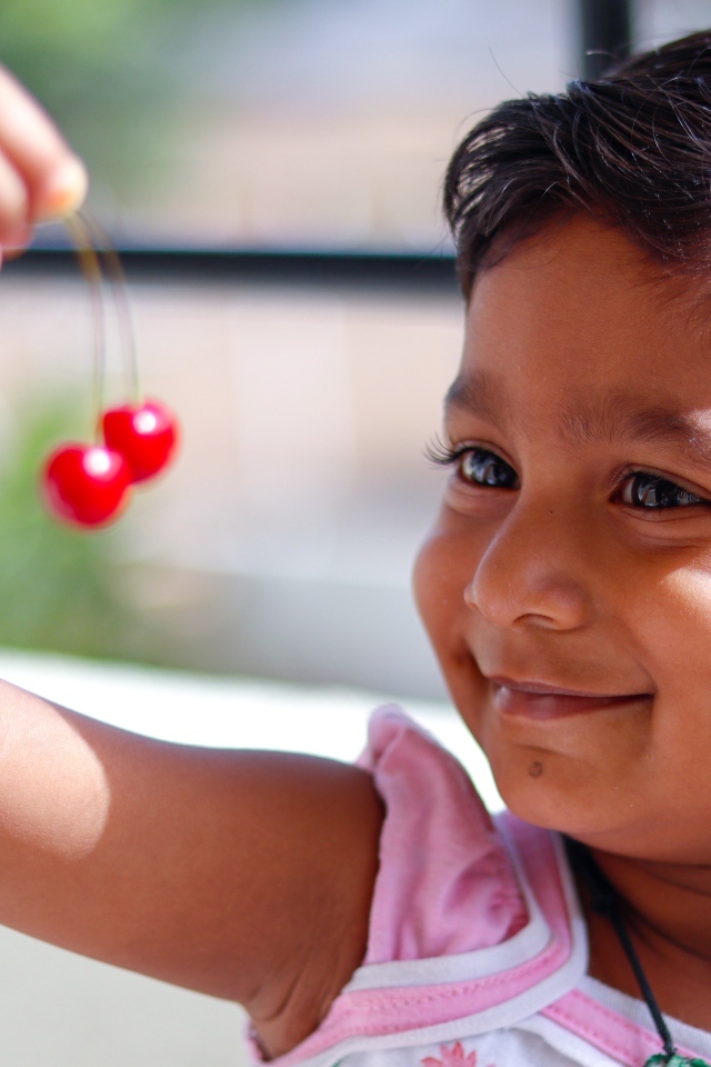 Маленькая улыбающаяся девочка с ягодами вишни в руках