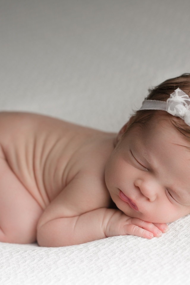 Новорожденная малышка с белой лентой на голове