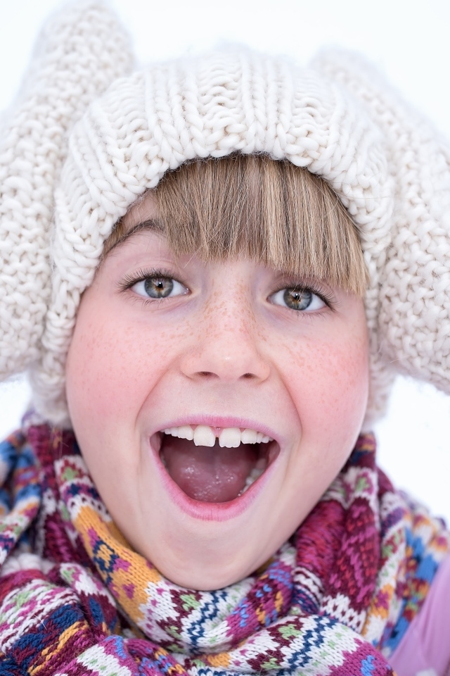 Довольная девочка в вязаной шапке и варежках