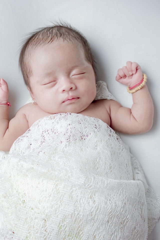 Маленький спящий ребенок на сером фоне под белым покрывалом