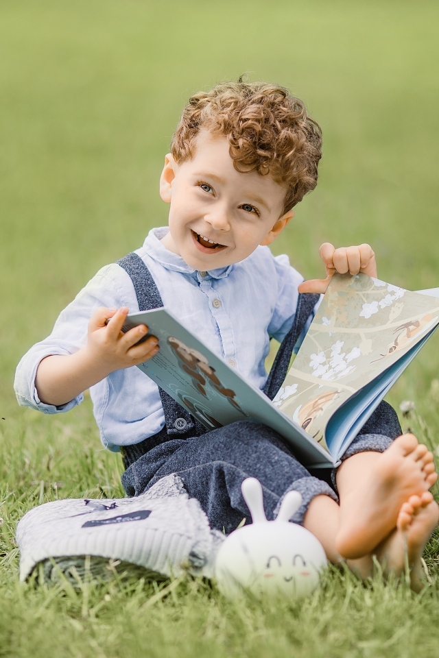 Улыбающийся мальчик с книгой сидит на траве
