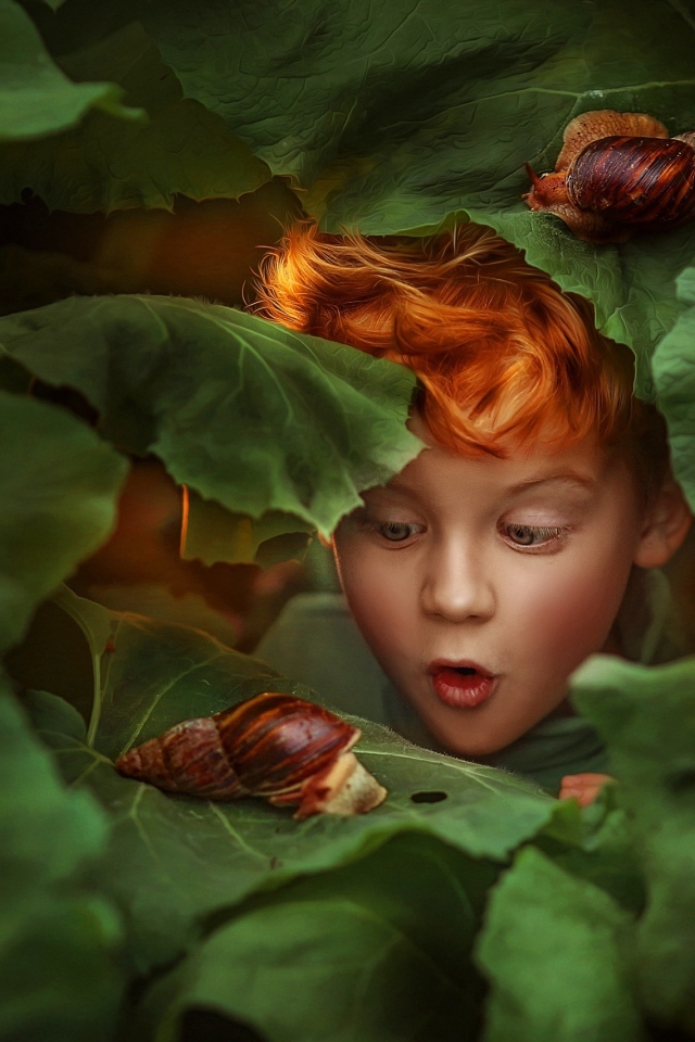 Удивленный рыжеволосый мальчик смотрит на улитку
