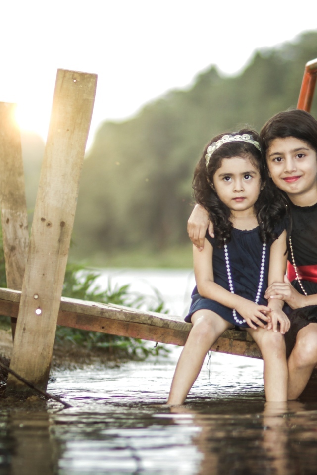 Две девочки сидят на мосту у реки
