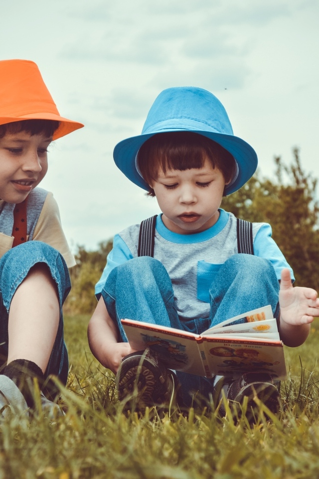 Два маленьких мальчика с книгой сидят на траве