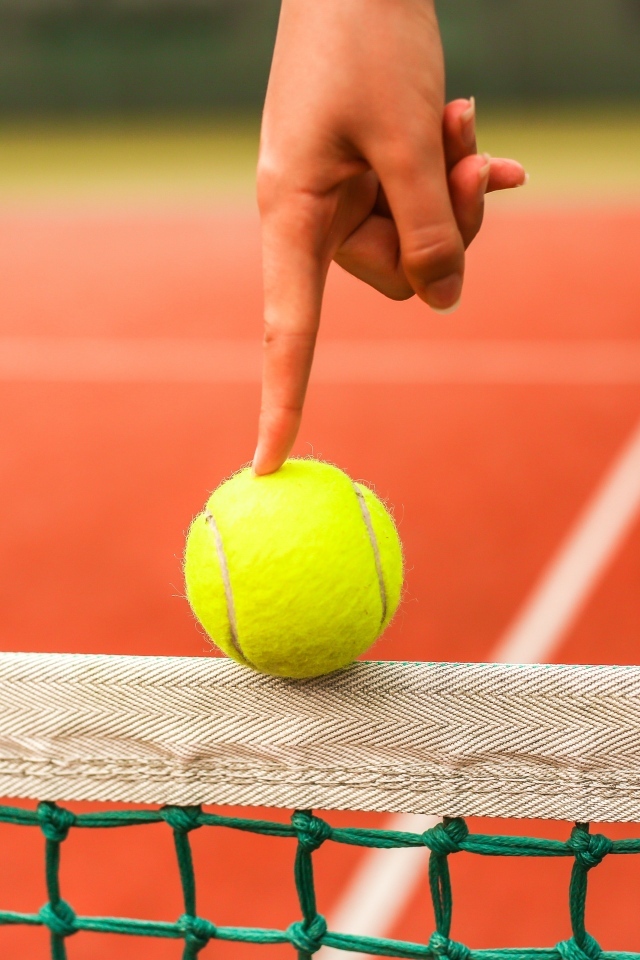 Палец держит желтый теннисный мяч