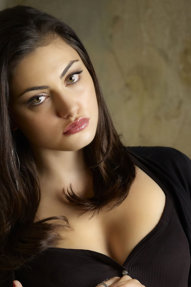 Actress Phoebe Tonkin stands against a wall in black