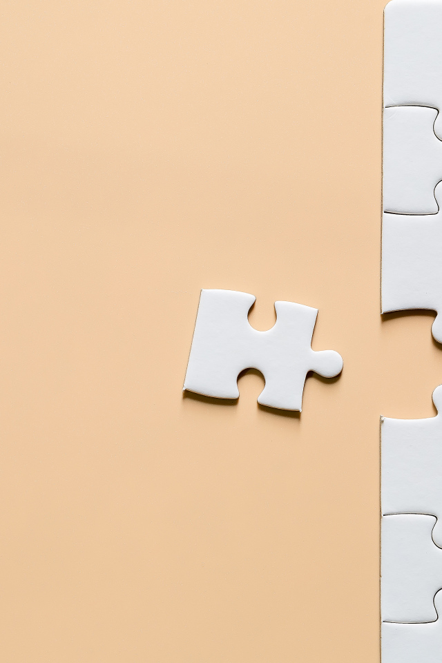 Белый пазл собирают на бежевом фоне
