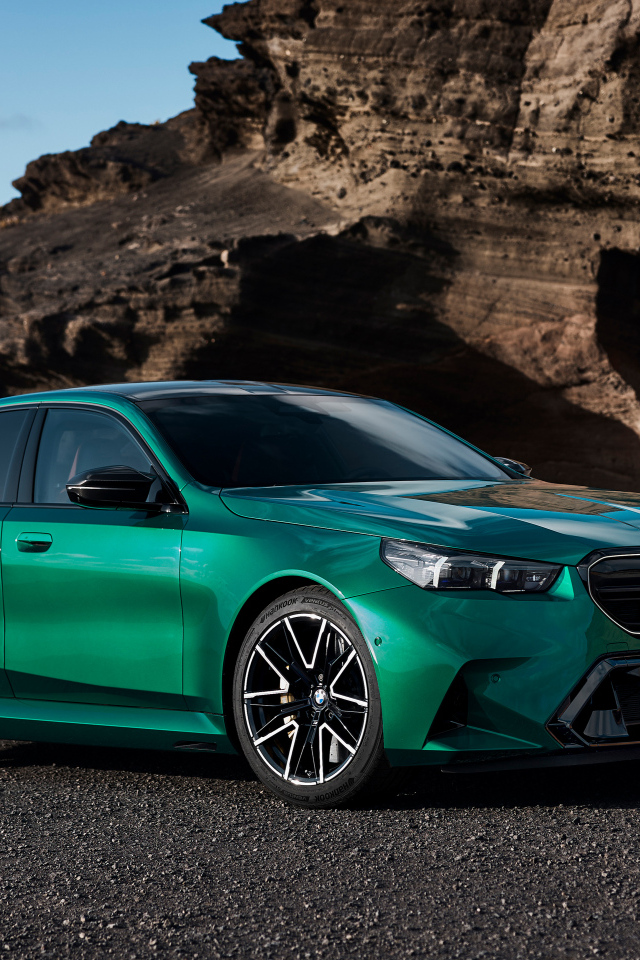 Зеленый автомобиль BMW M5 2024 года на фоне гор