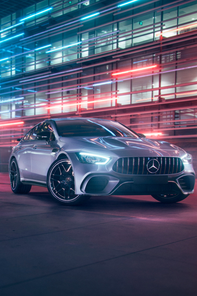 Серебристый автомобиль Mercedes AMG GT4 на фоне здания