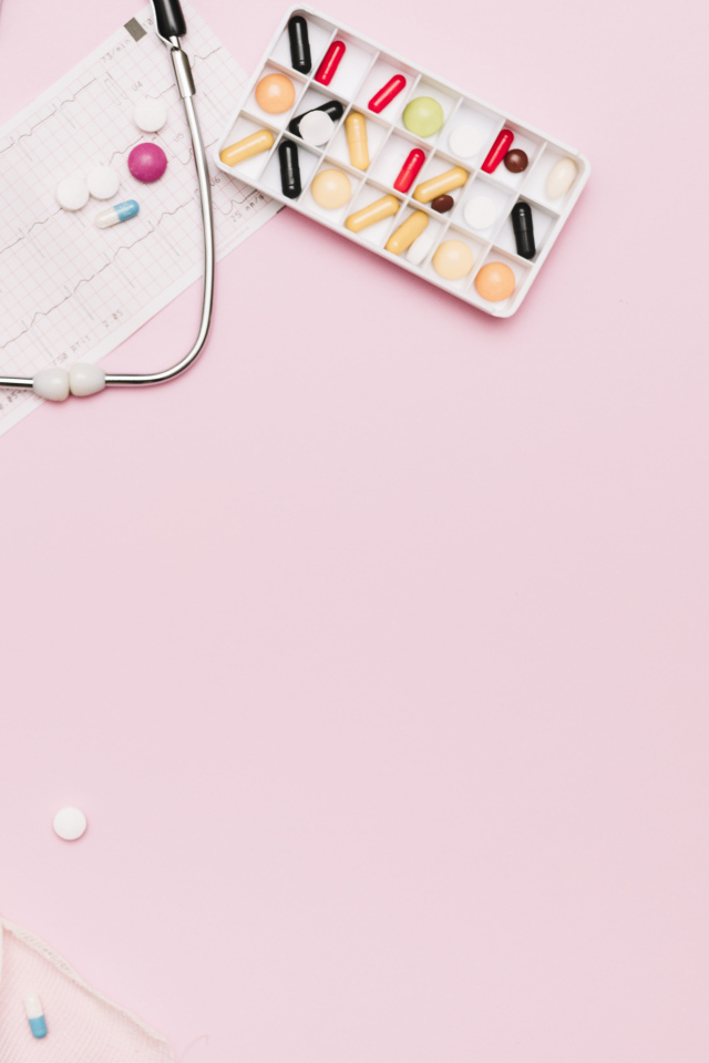 Стетоскоп и лекарства на кардиограмме на розовом фоне