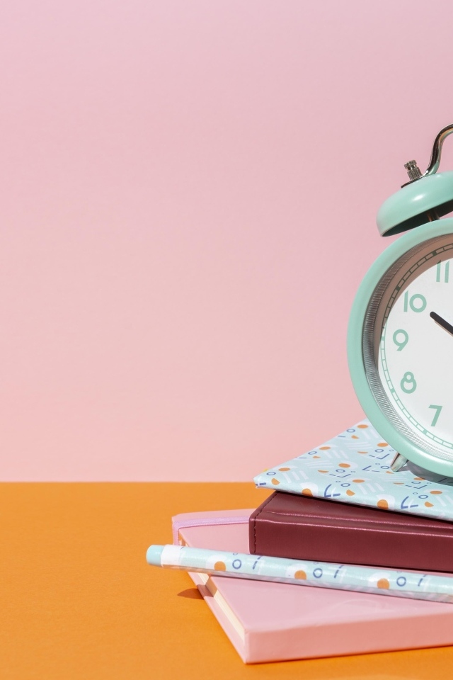 Будильник с книгами на розовом фоне