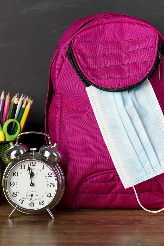 Рюкзак на столе с будильником, ручками и яблоком