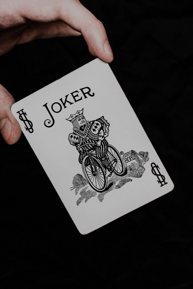 Карта Джокер в руке на черном фоне