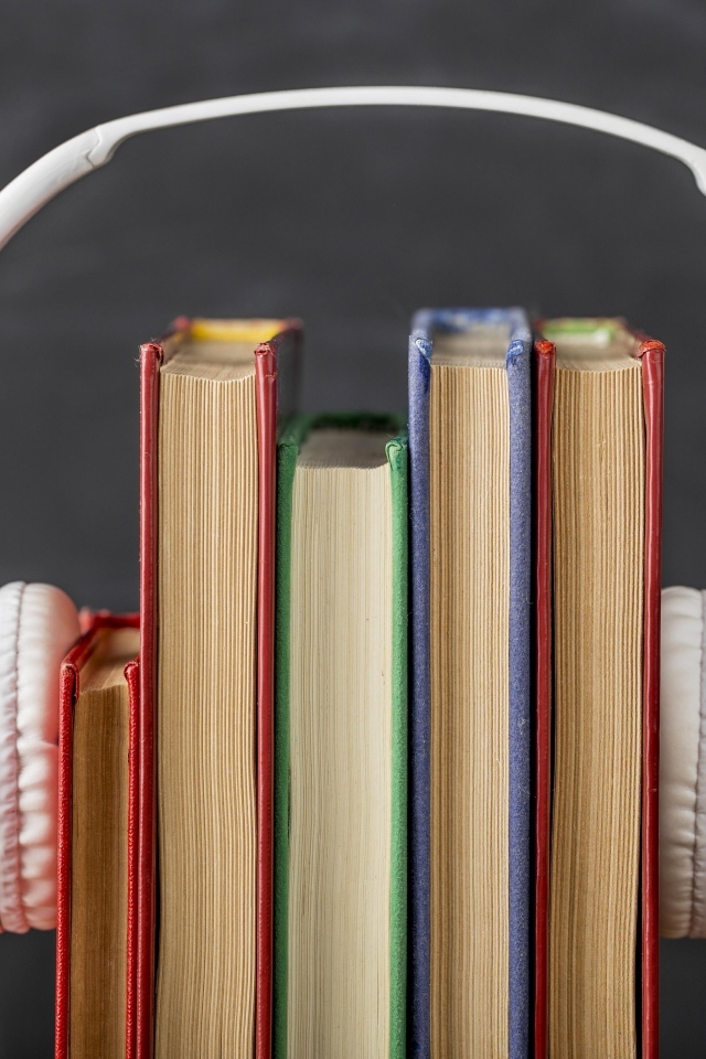 Разноцветные книги с белыми наушниками на сером фоне