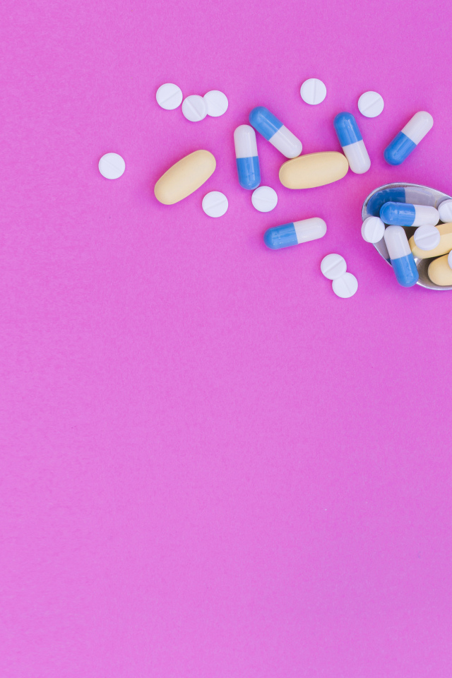 Таблетки с ложкой на розовом фоне