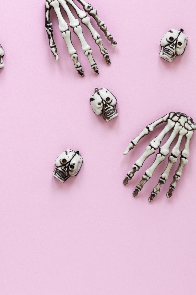 Кисти рук скелета и черепа на розовом фоне
