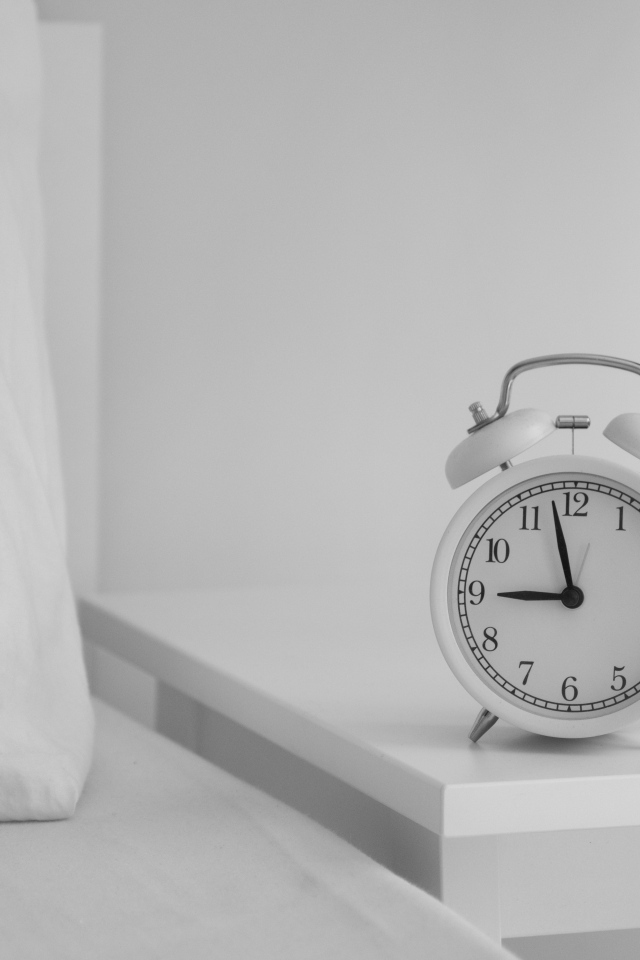 Будильник стоит на тумбочке у кровати 