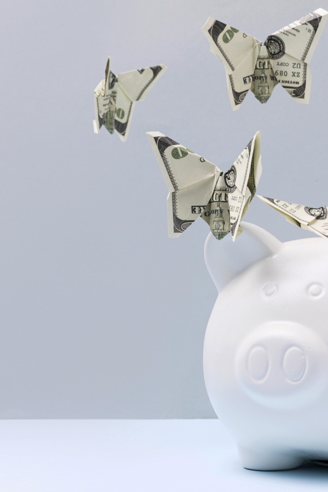 Свинья копилка с бабочками из купюр на сером фоне