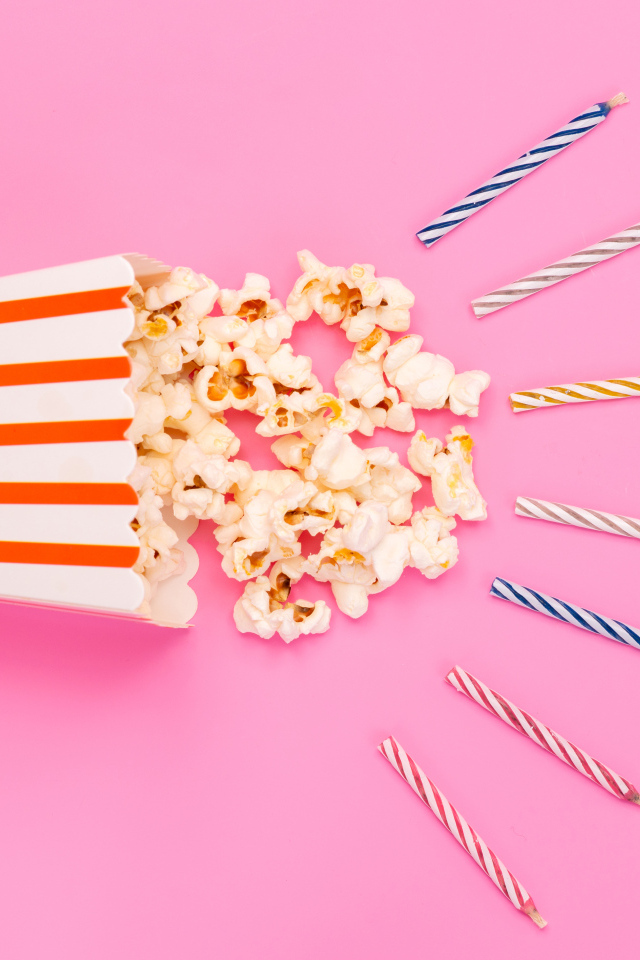 Коробка попкорна со свечами на розовом фоне