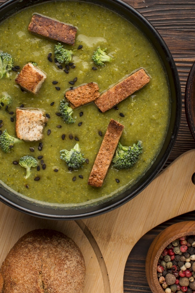 Зеленый суп пюре на столе с сухариками и перцем