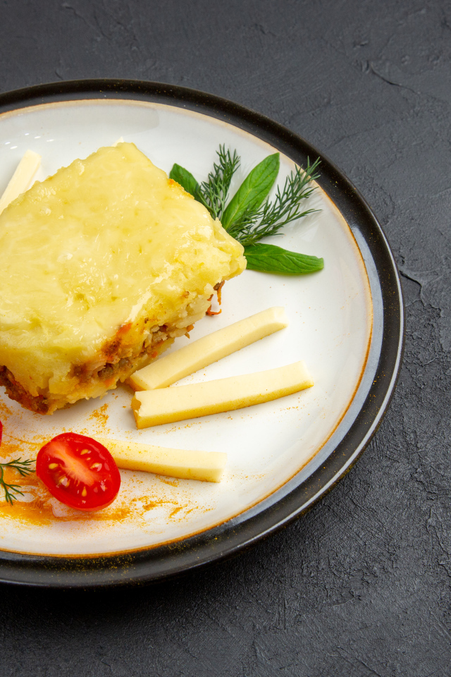 Кусок картофельной запеканки на тарелке с помидорами