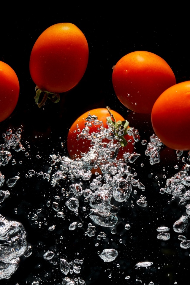 Красные помидоры в воде на черном фоне