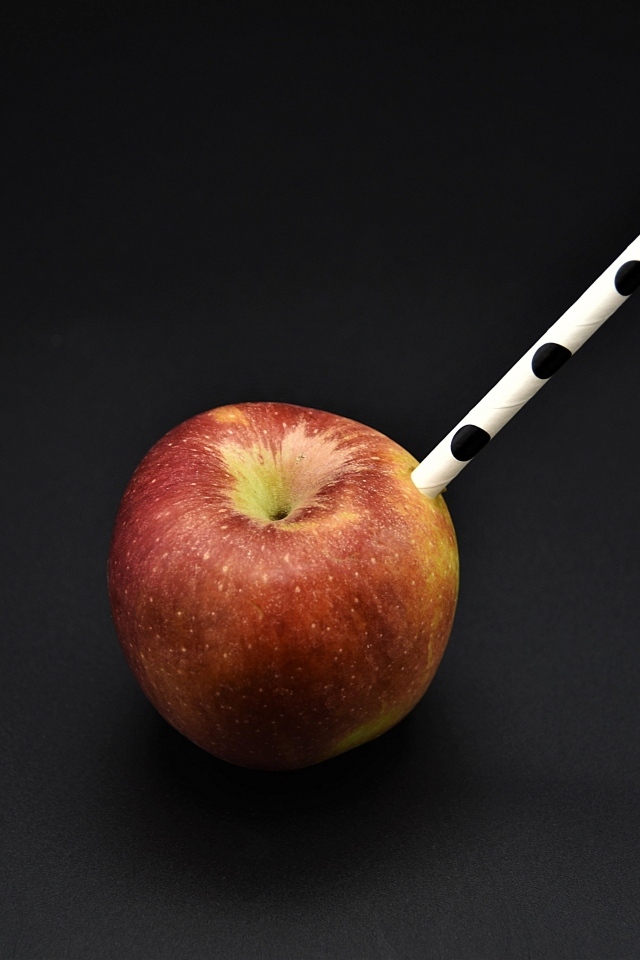 Большое красное яблоко с трубочкой на черном фоне