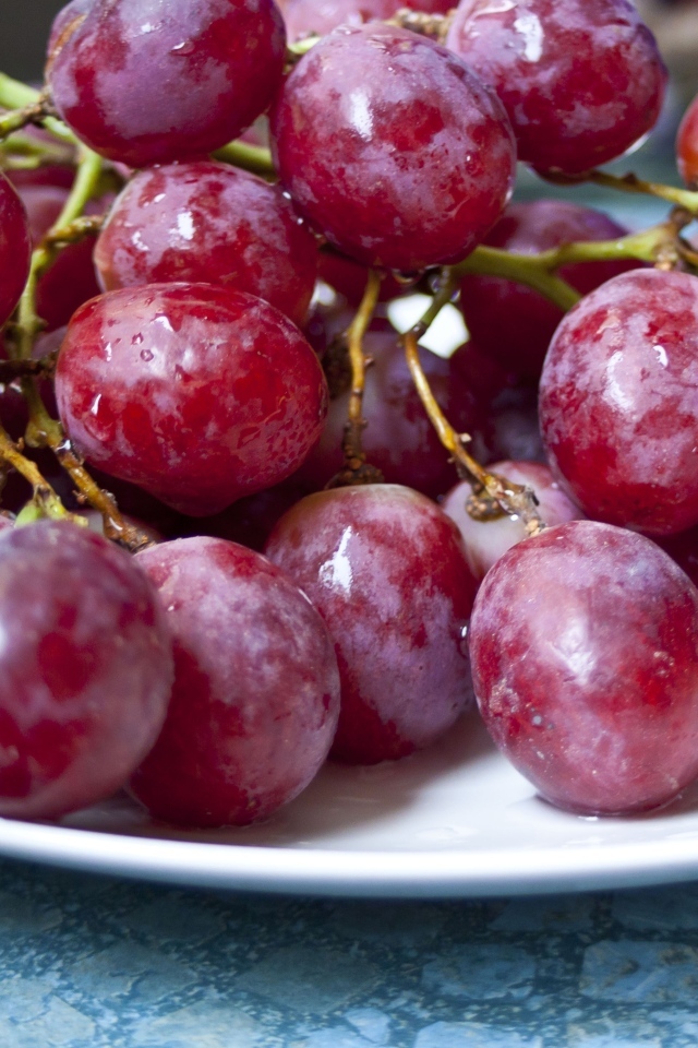 Спелый розовый виноград на белой тарелке