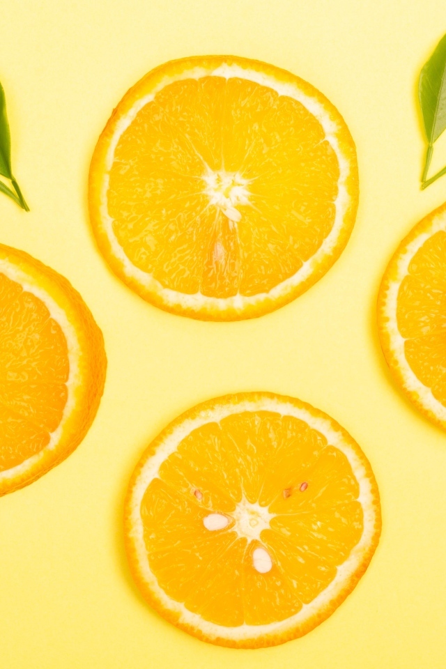 Нарезанный апельсин с зелеными листьями на желтом фоне