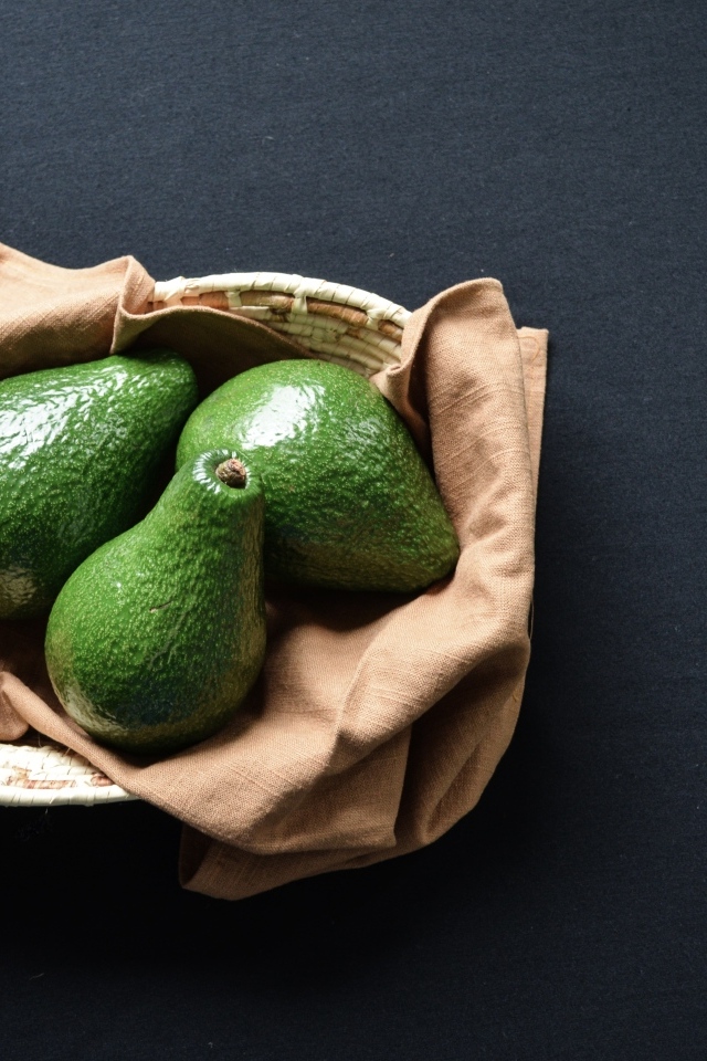 Три зеленых авокадо в корзинке на столе