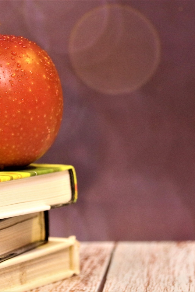 Мокрое яблоко на столе с книгами